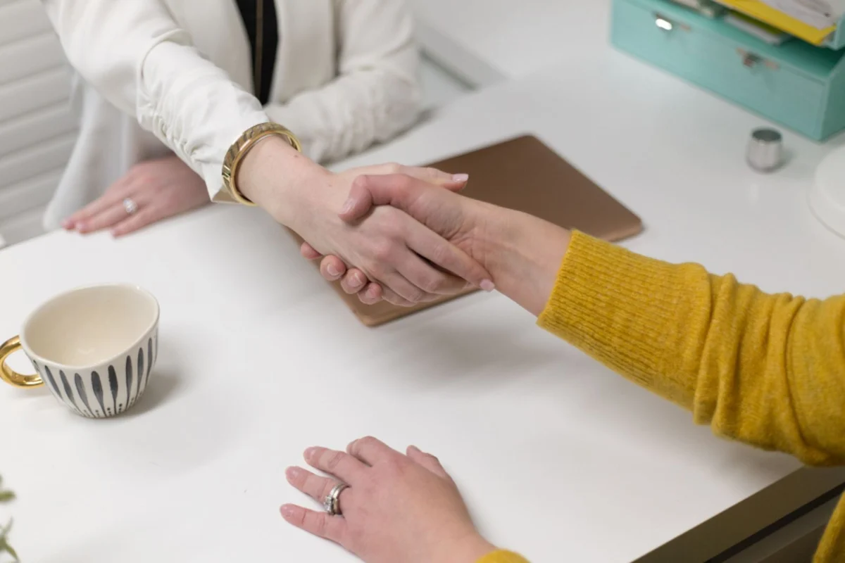 Zwei Menschen reichen sich über einen Schreibtisch die Hand